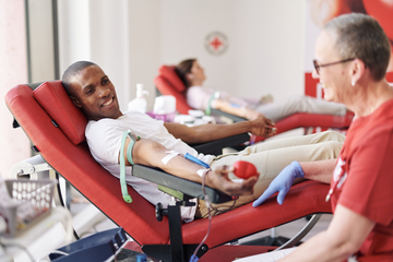Lächelnder Mann spendet Blut in einem Liegestuhl, während eine medizinische Fachkraft ihn überwacht